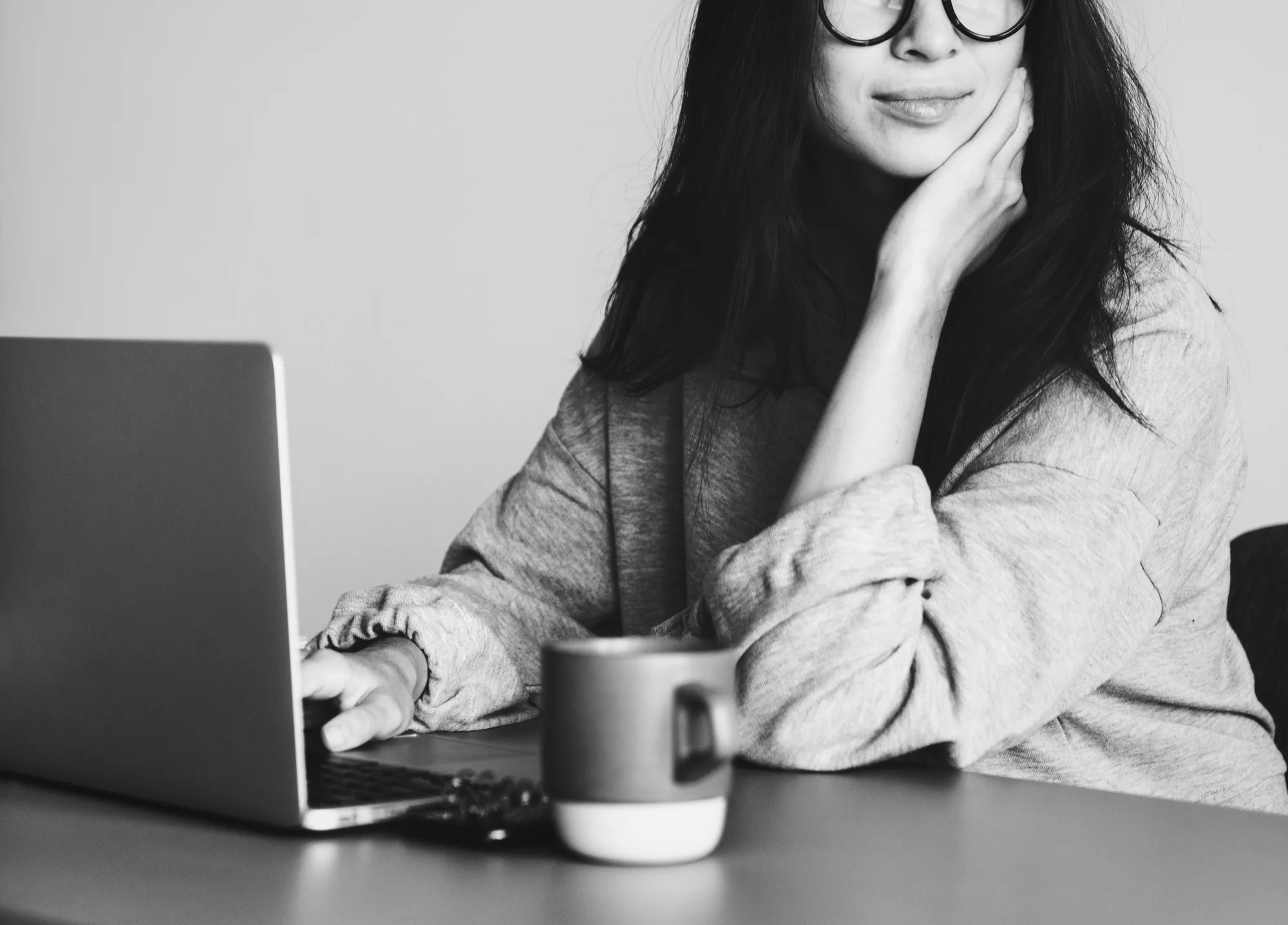 woman working on a laptop, wears glasses, coffee mug