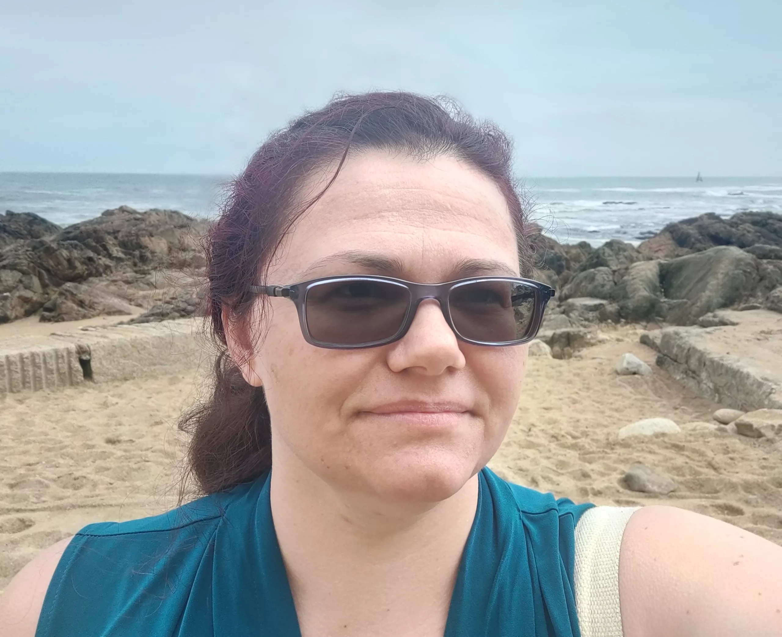 a woman in glasses taking a selfie on a rocky beach