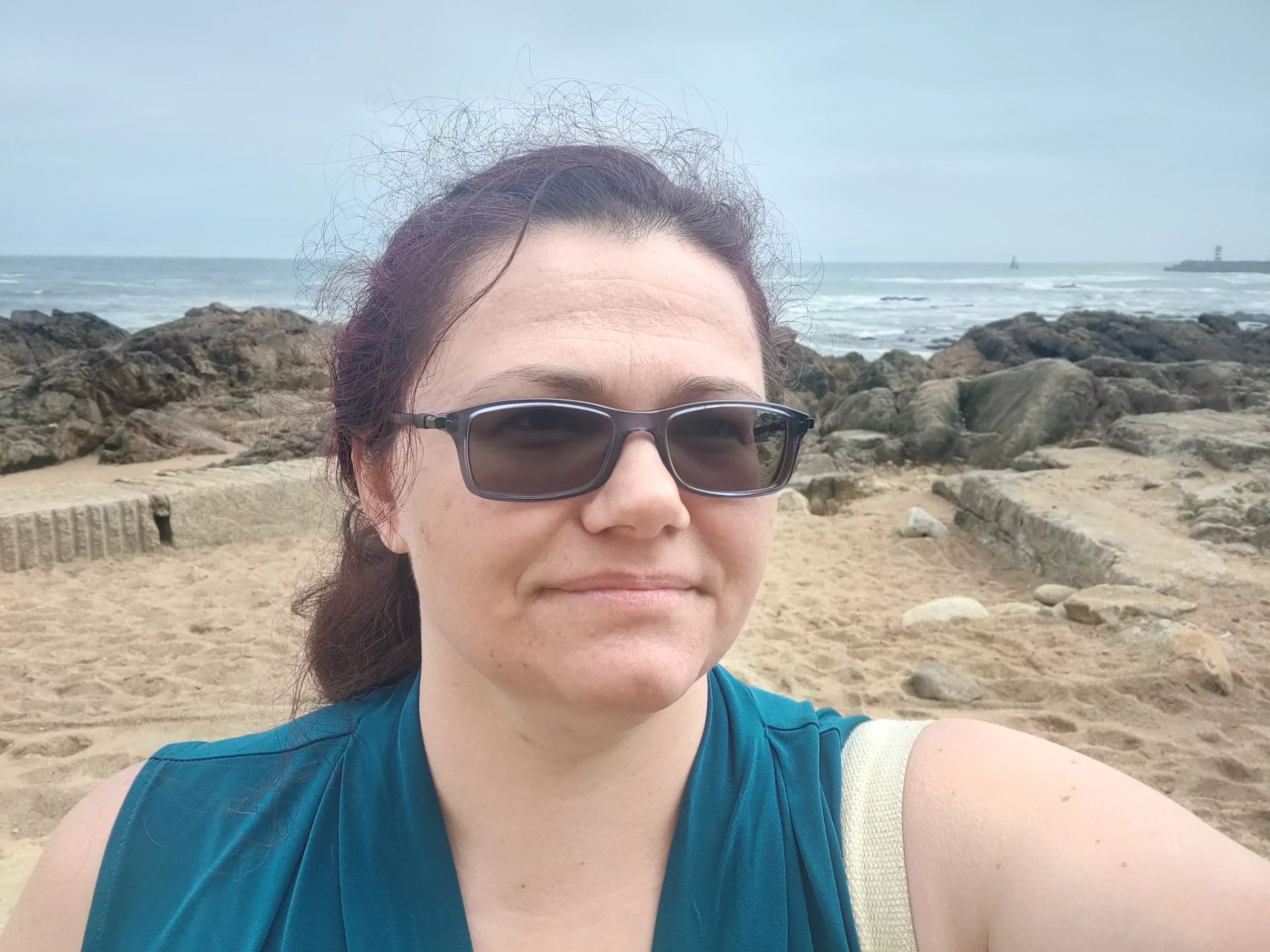 a woman in glasses taking a selfie on a rocky beach