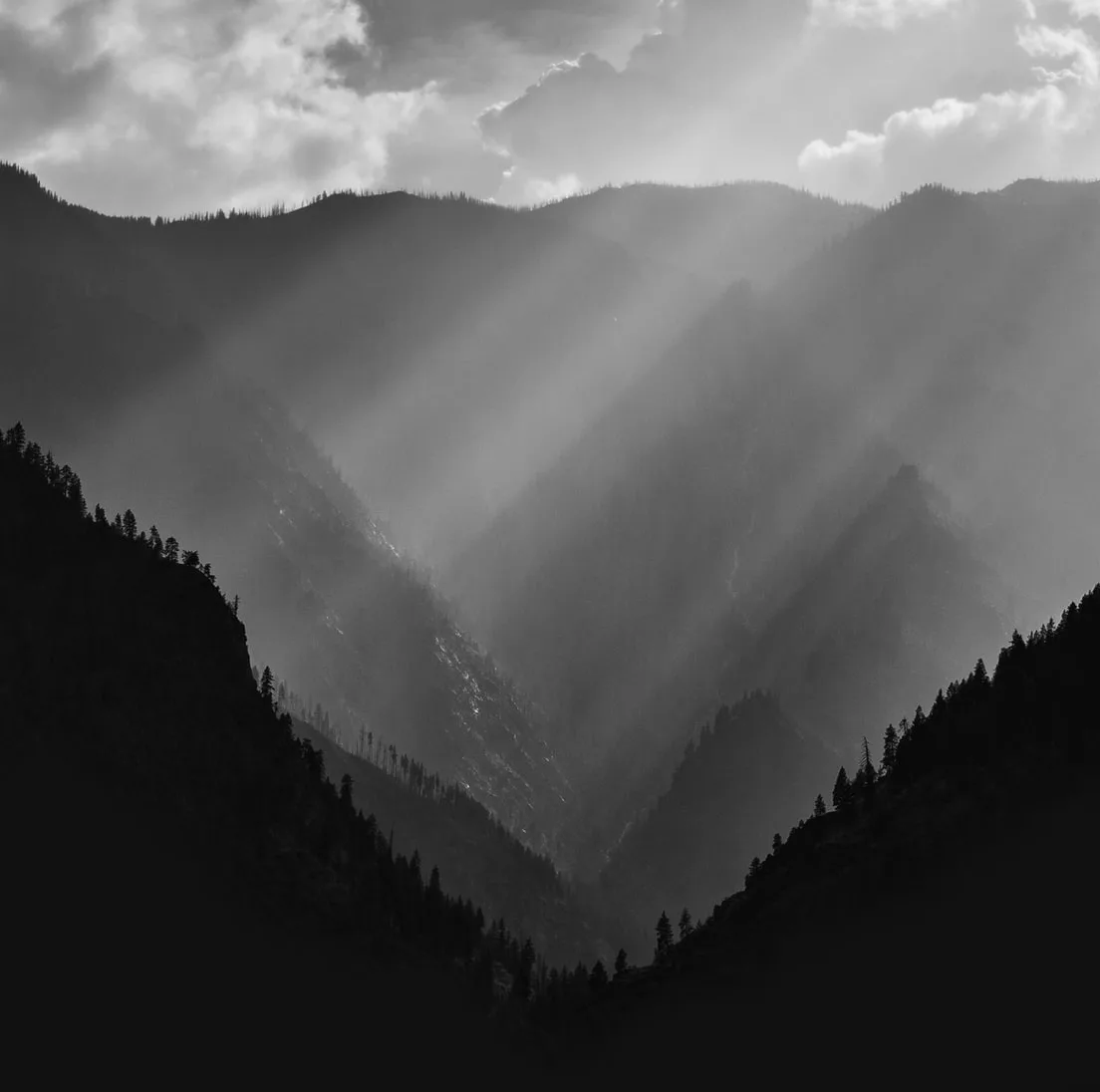ravine and mountains in the background with sun rays cutting through the fog